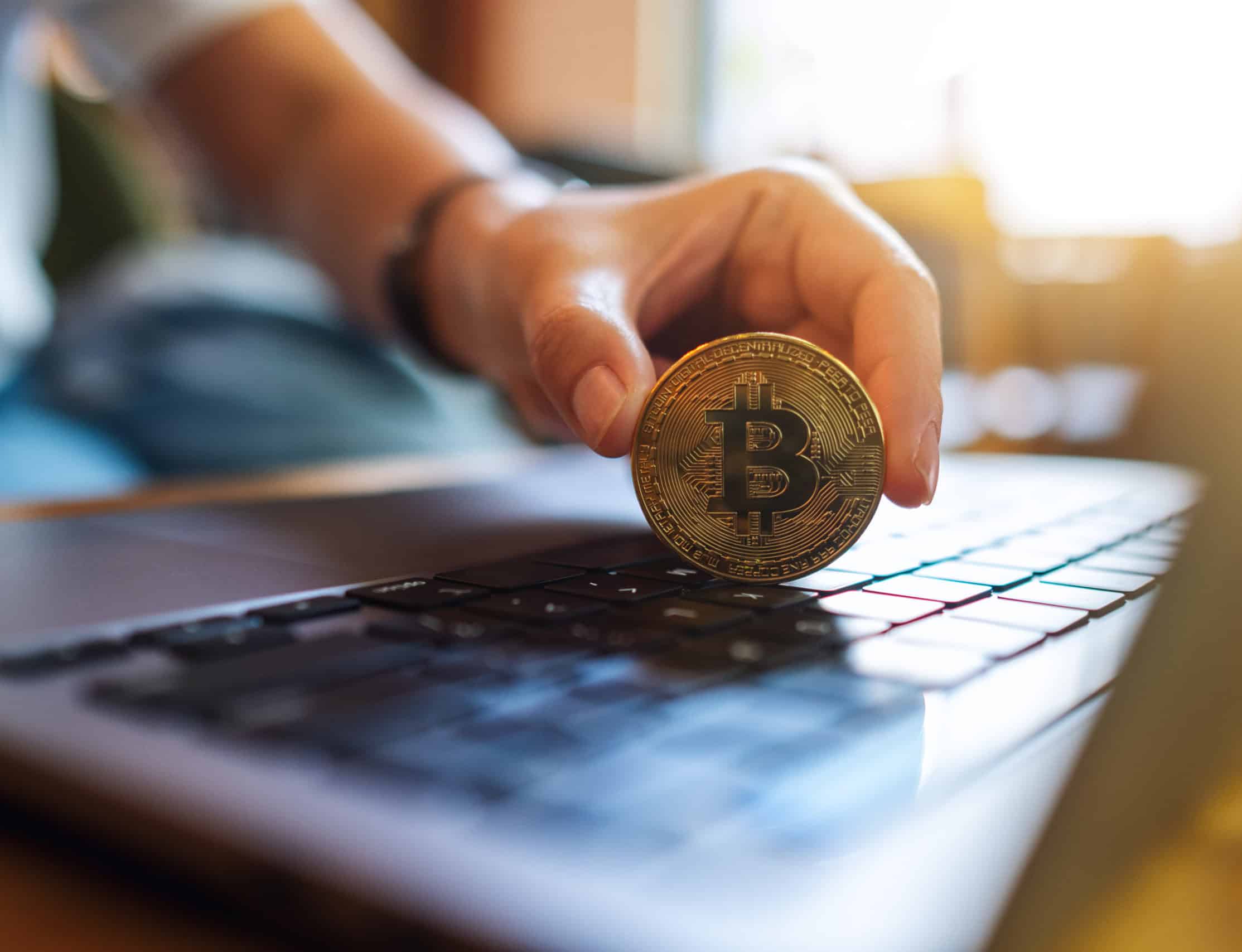 person holding bitcoin on top of laptop keyboard